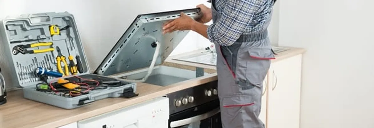 Cooktop repair technician lifting a built-in stovetop for service in Boise, ID